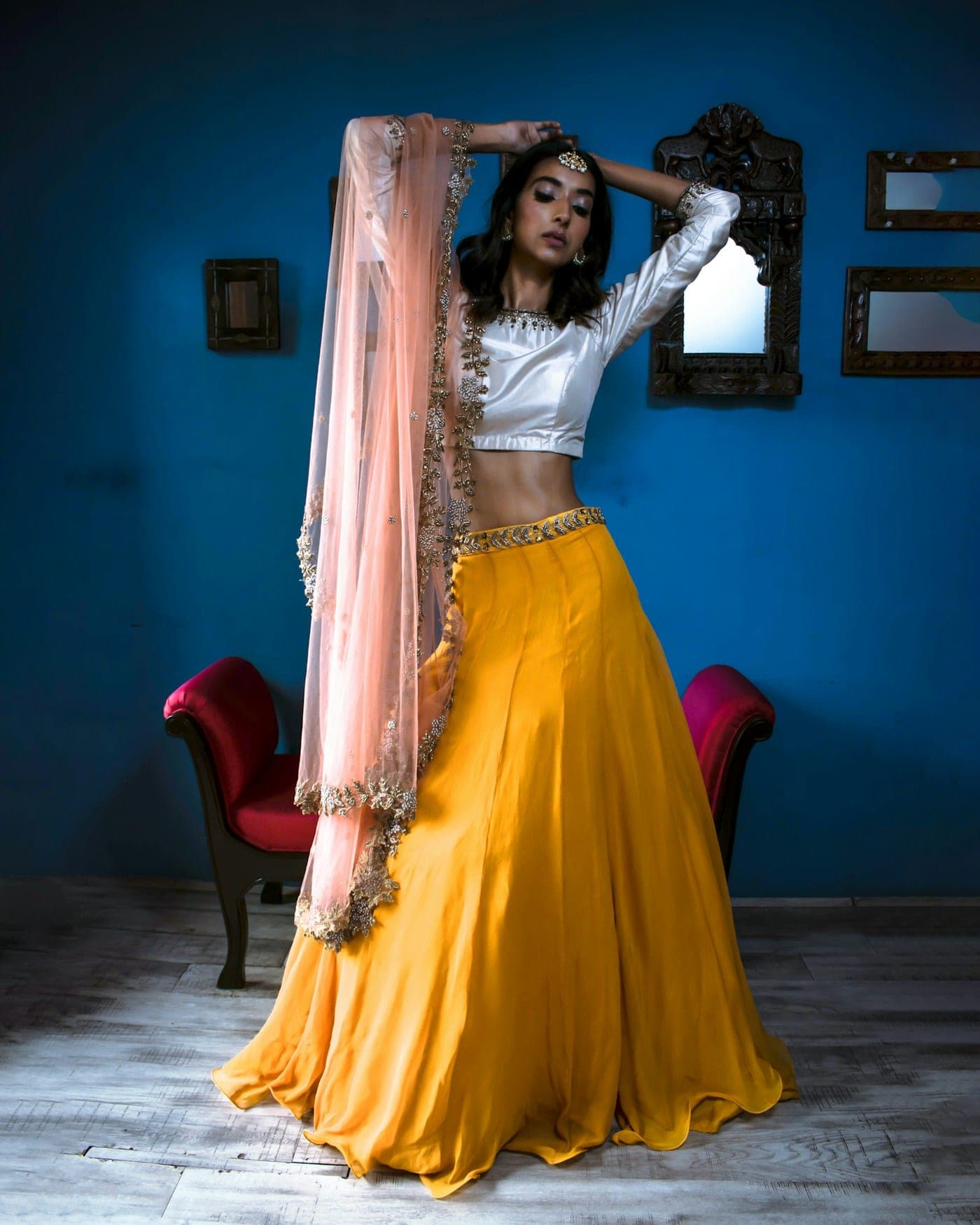 Woman in a marigold lehenga skirt and white blouse against a blue wall
