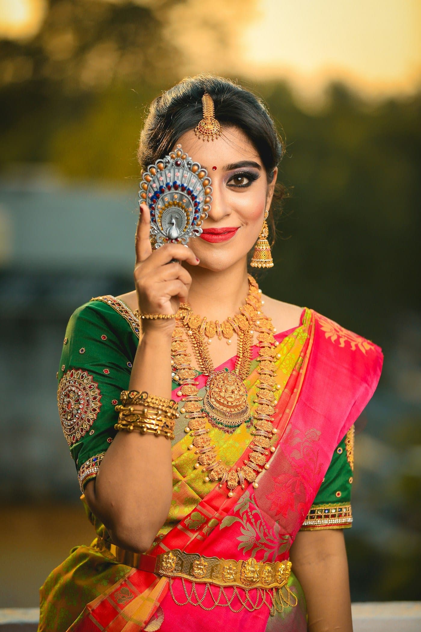 Woman in a pink and green silk saree holding a decorative fan