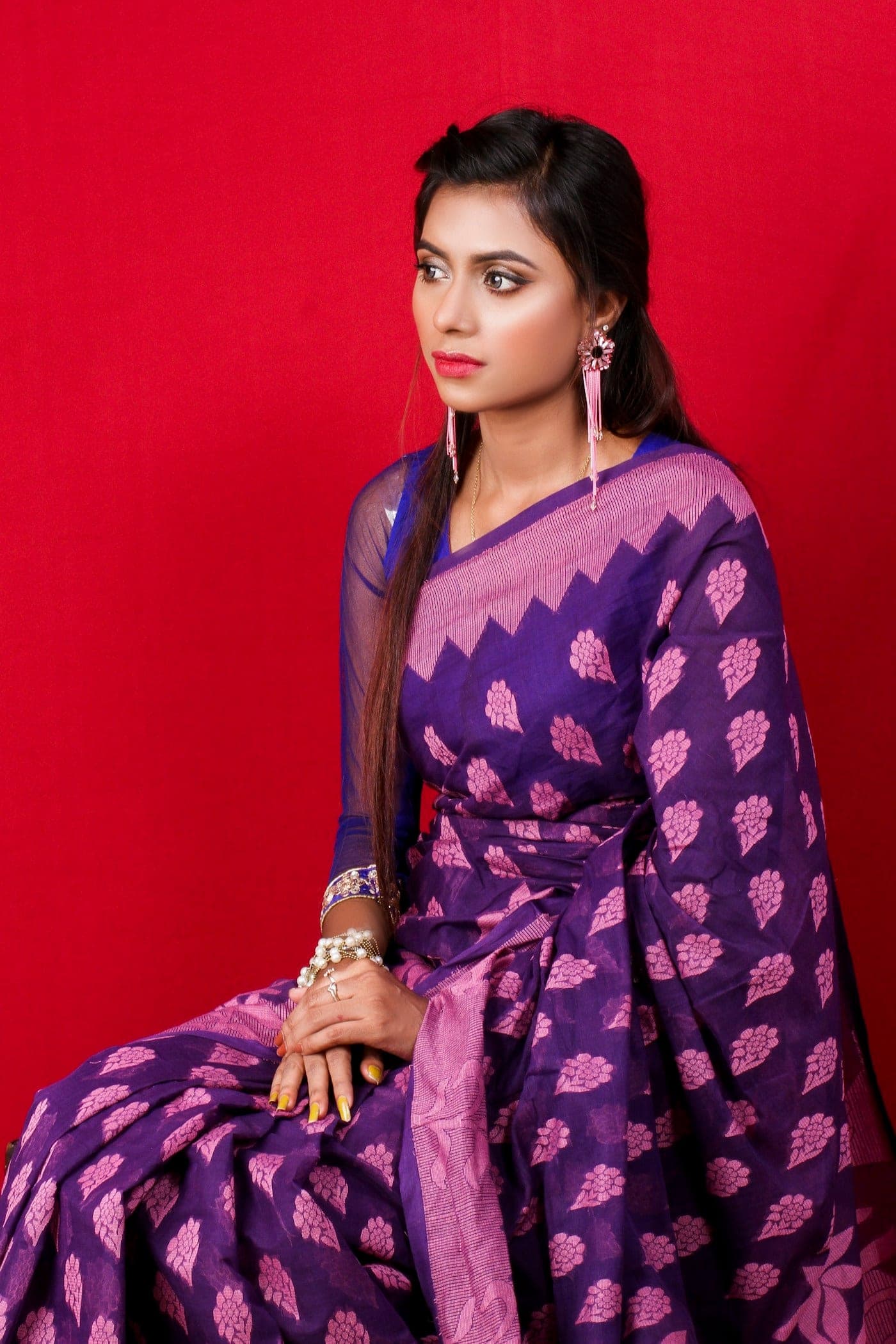 Woman in a violet woven saree against a red backdrop