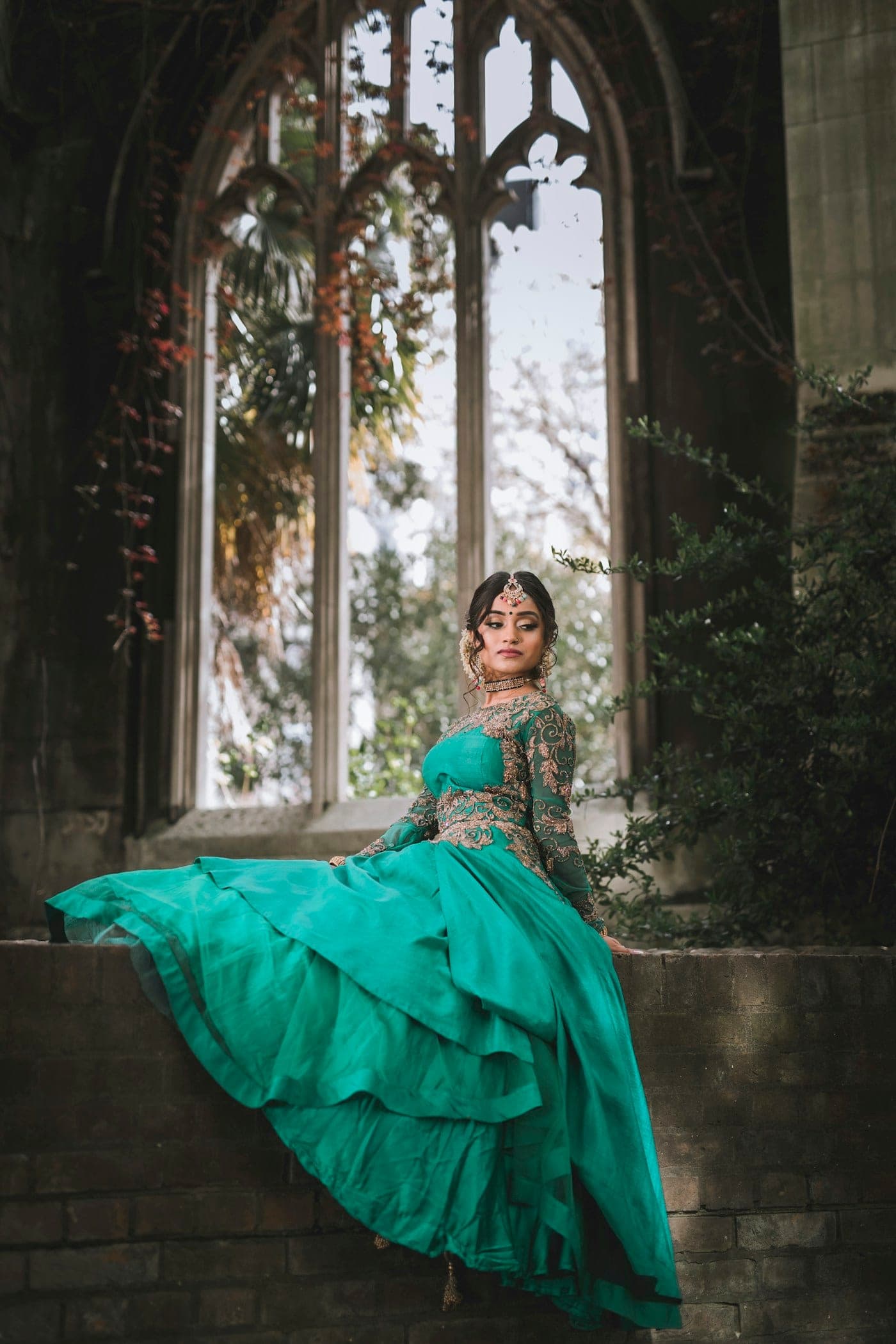 Woman in a teal tiered lehenga seated by an arched window